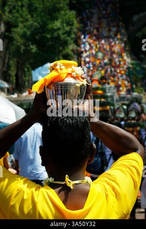 Vue arrière d'un pèlerin portant un pot sur la tête pendant le festival Thaipusam dans la campagne. L'image transmet la cérémonie culturelle et la tradition dans un cadre rural. Idéal pour les festivals culturels, la spiritualité et le contenu de voyage. Banque D'Images