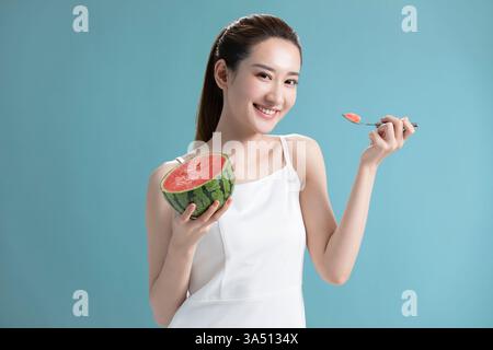Belle jeune femme chinoise appréciant une tranche de pastèque. Image de style de vie fraîche et dynamique idéale pour une alimentation saine, un style de vie estival et des images de fruits. Idéal pour la nourriture, le bien-être et les contextes de mode décontractés. Banque D'Images