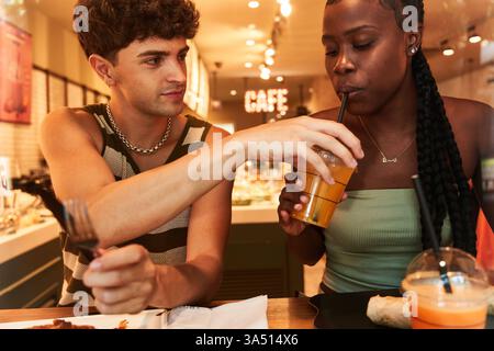 Femme noire aime le jus avec une paille partagée par son petit ami caucasien sur une table de restaurant. Cette scène de couple diversifiée fonctionne bien pour les repas, les rencontres et les promotions de style de vie. Banque D'Images