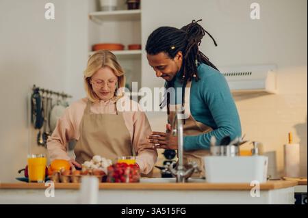 Les partenaires sont debout dans la cuisine et préparent un repas végétarien sain ensemble à la maison. Le couple fait un déjeuner maison ensemble à la maison. Banque D'Images