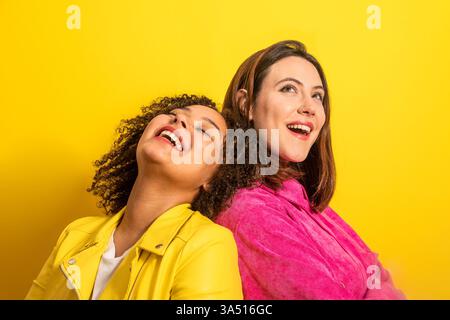 Femme noire avec les yeux fermés penchant la tête sur le dos d'une amie féminine caucasienne debout près l'un de l'autre sur fond jaune en studio Banque D'Images