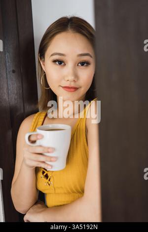 Portrait décontracté d'une femme élégante appuyée contre un mur avec une tasse. Parfait pour la culture du café, la mode de rue et les visuels de la vie urbaine quotidienne. Banque D'Images