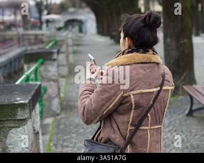 Femme hispanique en plein air prend des photos avec un smartphone, capturant des moments de voyage. Cette image de concept de voyage convient au tourisme, à la photographie et au contenu de style de rue. Banque D'Images