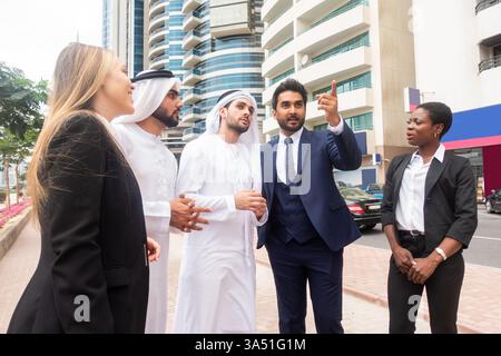 Groupe diversifié de gens d'affaires marchant à l'extérieur dans une ville des Émirats arabes Unis, parlant du travail. La scène exprime le travail d’équipe et la collaboration multiculturelle dans un environnement urbain moderne. Idéal pour les entreprises, le réseautage et les campagnes d'entreprise. Banque D'Images