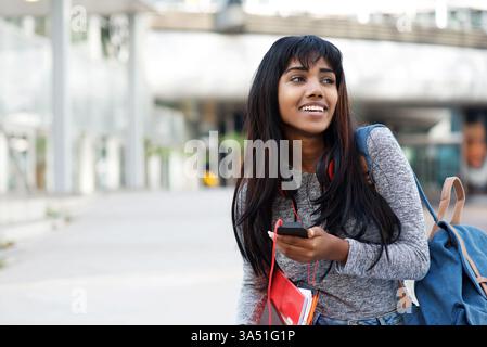 Portrait d'un heureux étudiant indien marchant dehors avec un téléphone portable. La scène capture la vie sur le campus, la jeunesse et la connectivité pour des thèmes liés à l'éducation ou à la technologie. Idéal pour la vie étudiante, l'apprentissage numérique et le marketing sur campus. Banque D'Images
