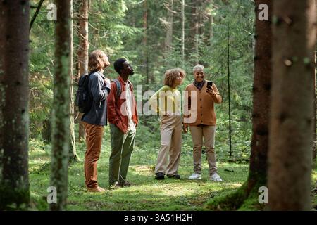 Groupe d'amis divers en plein air, randonnée dans une forêt et profiter de la nature. Ils se tiennent sur une pelouse, examinant un smartphone ensemble pour une ambiance de voyage ou d'aventure en plein air. Parfait pour le style de vie, les voyages et les thèmes de l'amitié dans les environnements de la nature. Banque D'Images