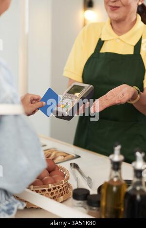 Gros plan de caissière asiatique traitant un paiement par carte dans un café avec un lecteur de carte. La scène met en évidence le paiement au détail et le paiement sans espèces. Utile pour l'hôtellerie, le point de vente et le contenu des petites entreprises. Banque D'Images