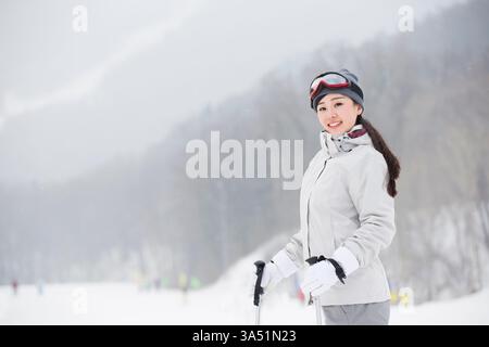 Portrait d'une jeune skieuse chinoise en plein air dans une station d'hiver. L'image transmet la joie et la confiance dans un cadre enneigé et alpin, parfait pour les voyages, les vacances et les campagnes de sports d'hiver. Un portrait focal propre adapté au style de vie et au marketing sportif mettant en vedette des athlètes féminines asiatiques. Banque D'Images