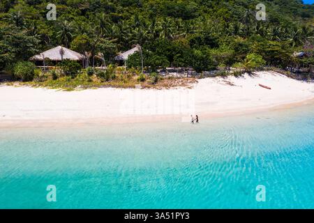 Femme asiatique marchant main dans la main avec son petit ami caucasien le long d'une plage tropicale à Palawan, Philippines, pendant l'été. Idéal pour les voyages et les campagnes en couple, capturant une ambiance balnéaire paradisiaque avec de l'eau turquoise, du sable blanc et une rive bordée de palmiers. Banque D'Images
