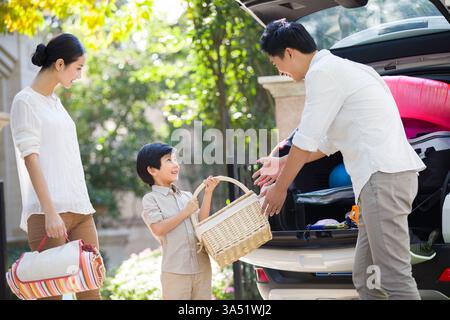 Jeune famille chinoise profitant d'un pique-nique en plein air, rayonnant de bonheur et de convivialité. Une scène de style de vie joyeuse parfaite pour la famille, les voyages et les activités de week-end. Idéal pour les histoires sur les ménages chinois modernes et les loisirs de plein air. Banque D'Images