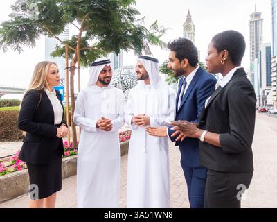 Groupe diversifié de professionnels des affaires marchant et parlant dans un cadre urbain des Émirats arabes Unis. Idéal pour les affaires internationales, le travail d'équipe et les communications d'entreprise multiculturelles. Banque D'Images