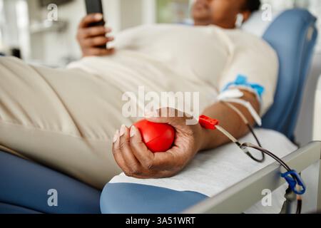 Gros plan d'une jeune femme noire dans un centre de don de sang, pressant une balle de stress pour rester calme pendant la procédure. Cette image des soins de santé met en valeur les dons, les soins aux patients et le soutien communautaire vital. Banque D'Images
