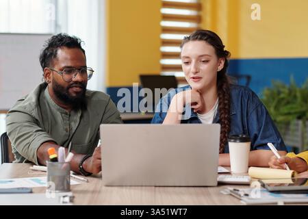 L'équipe d'affaires diversifiée dynamique discute d'un graphique sur un écran d'ordinateur portable et planifie les prochaines étapes dans un environnement de bureau. Idéal pour le travail d'équipe, la collaboration et les visuels de planification d'entreprise. Banque D'Images