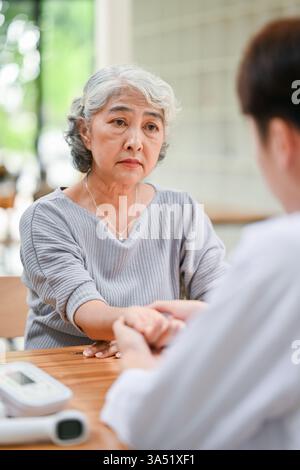 Femme aînée asiatique subissant un examen médical en tant que médecin vérifie son pouls à l'hôpital. La scène met en lumière les soins de santé, les soins aux aînés et les consultations médicales attentionnées. Adapté aux soins de santé, aux communications hospitalières et aux sujets de bien-être. Banque D'Images