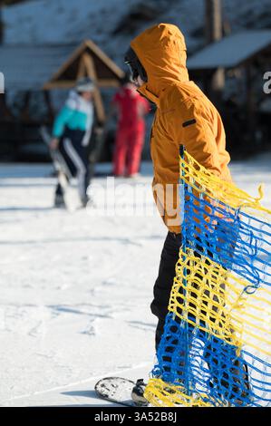 Un snowboarder se prépare pour une descente exaltante sur les pistes, vêtu d'une veste orange vif. À proximité, les skieurs s'engagent dans une joyeuse activité hivernale Banque D'Images