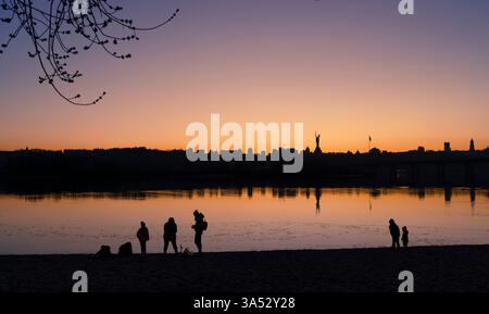 Kiev, Ukraine - 20 mars 2025 : les gens se reposent à la plage, de la rivière Dnipro , contre la vue panoramique du célèbre monument mère Ukraine - symbole de la lutte ukrainienne face à l'invasion russe à grande échelle en Ukraine ( 24 février 2022) et une partie du Musée national de l'histoire de l'Ukraine dans la seconde Guerre mondiale. Creadit : Artem Hvozdkov / Alamy news Banque D'Images