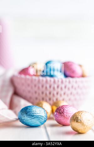 Oeufs de pâques en chocolat enveloppés dans une feuille multicolore sur une table blanche. Banque D'Images