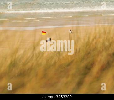 Regardant à travers l'herbe marram au-dessus de Hayle Beach, Cornwall Angleterre jusqu'à un maître nageur assis avec la natation et pas de drapeaux de natation Banque D'Images
