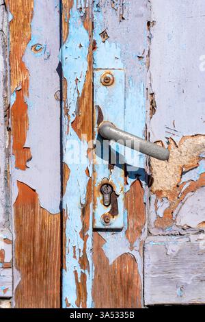 Une porte en bois vieilli affiche une peinture bleu écaillé et une poignée rouillée, mettant en valeur des années d'exposition aux éléments. La porte est affligée de l'appearanc Banque D'Images