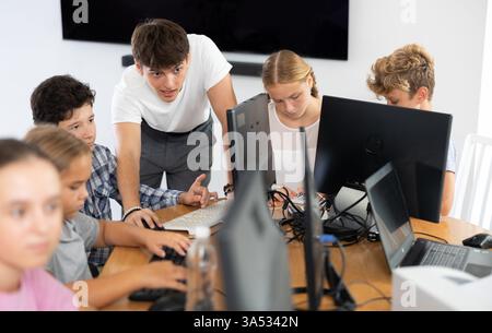 Enseignant homme positif avec le garçon enseigne comment travailler sur ordinateur Banque D'Images