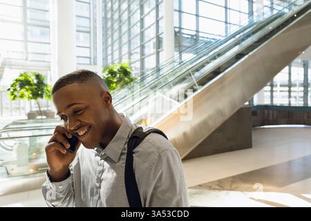 Homme d'affaires parlant sur smartphone, souriant tout en marchant dans le centre de conférence moderne, espace de copie Banque D'Images