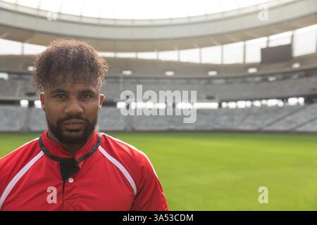 Joueur de rugby en maillot rouge debout en toute confiance dans le stade vide, espace de copie Banque D'Images