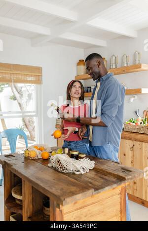 Couple diversifié préparant le repas dans la cuisine, souriant et profitant du temps ensemble Banque D'Images