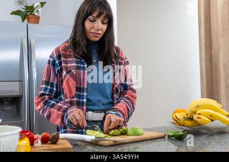 Jeune femme préparant un repas sain en tranchant de l'avocat frais sur une planche à découper dans une cuisine moderne Banque D'Images