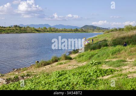 Gwangju, Corée du Sud - 24 septembre 2020 : les gens pêchent le long des rives de la rivière Yeongsangang, ombragée par des parasols colorés, avec des collines et Banque D'Images