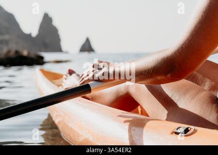 Kayak Ocean Coast femme relaxant - gros plan des mains de la femme sur une pagaie de kayak tout en kayak dans l'océan avec des falaises rocheuses en arrière-plan. Banque D'Images