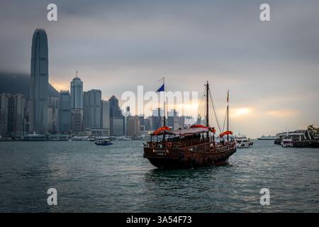 Hong Kong. Chine- 02.20.2025. Le bateau de croisière Chinese Junk, l'Aqua Luna, navigue dans le port de Victoria avec le coucher du soleil sur l'île de Hong Kong. Banque D'Images
