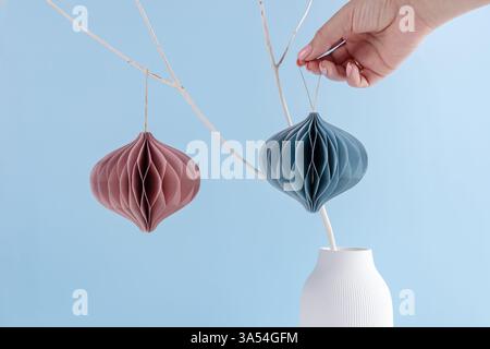 Ornements de Noël scandinaves minimalistes en nid d'abeille en papier sur un décor écologique de branche blanche sur fond bleu Banque D'Images