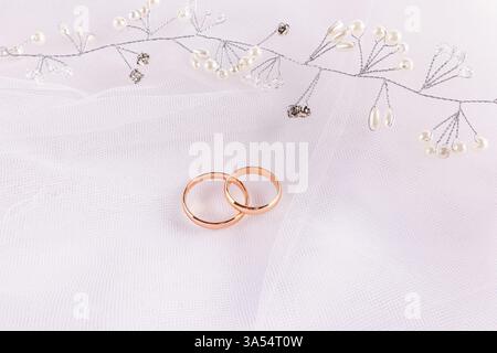 Un bel arrangement de mariage avec deux anneaux de mariage en or et une décoration de coiffure de perle et de strass. fond de tulle blanc Banque D'Images