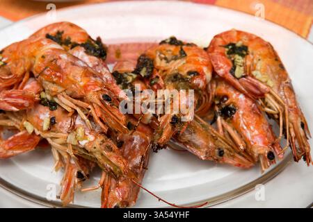 Gros plan de crevettes royales grillées avec leurs coquilles, empilées sur une assiette blanche. Leur texture dorée et juteuse met en valeur la saveur et la gourme des fruits de mer Banque D'Images