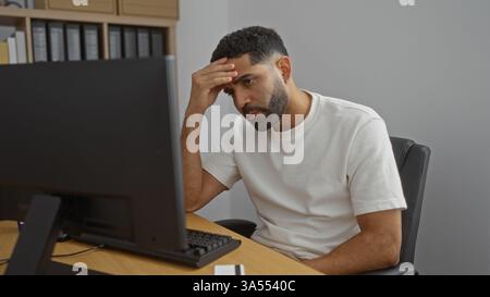 Jeune homme au bureau portant une chemise blanche, assis et regardant stressé à l'écran d'ordinateur Banque D'Images