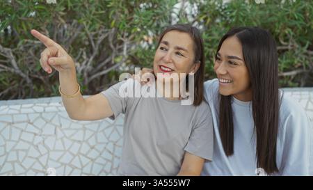 Mère et fille partageant un moment joyeux à l'extérieur, avec la mère pointant quelque chose au loin Banque D'Images