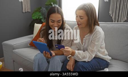Mère et fille souriant ensemble dans le salon, en utilisant la tablette et la carte de crédit, mettant en valeur l'amour de la famille, l'amitié et le cadre moderne de la maison avec WO Banque D'Images