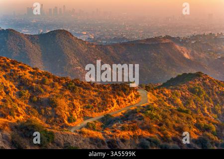 Routes de randonnée sinueuses dans Griffith Park avec vue sur le centre-ville brumeux de Los Angeles et l'observatoire Griffith au loin. Une lumière chaude allume le réseau local Banque D'Images