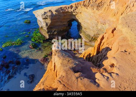 Superbe formation rocheuse côtière avec une arche naturelle, entourée de marées et d'algues vertes éclatantes, capturée à San Diego pendant l'heure dorée Banque D'Images
