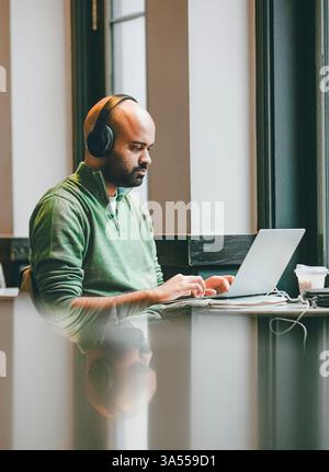 Un homme portant des écouteurs boit avec son reflet. Banque D'Images