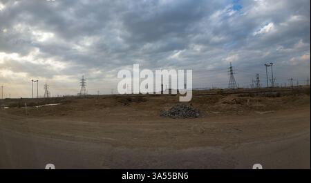 Un paysage aride avec des lignes électriques s'étendant à travers l'horizon sous un ciel nuageux. Le sol est sec et rocheux, avec un petit tas de pierres visible Banque D'Images