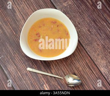Une assiette de soupe de pois chaude et savoureuse avec des viandes fumées sur une table en bois, une cuillère à proximité. Vue de dessus, pose à plat. Banque D'Images