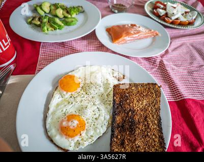 Brunch maison avec œufs frits, pain de seigle, tranches d'avocat, saumon et salade de fromage. Banque D'Images