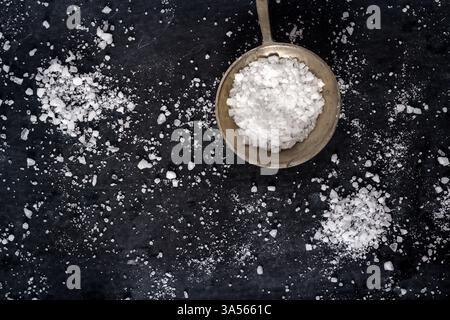 Vue de dessus d'une cuillère avec du sel de mer à grains grossiers sur fond noir. Pose à plat. Vue de dessus. Concept alimentaire. Banque D'Images