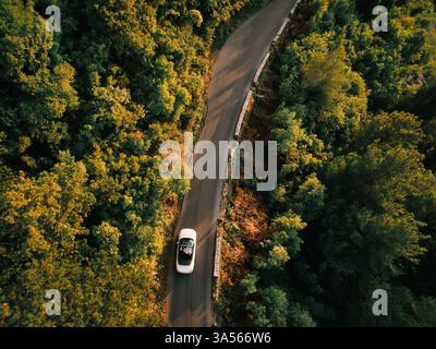 Montenegro, Kotor - 13 juillet 2024 : White Cabriolet roule le long d'une autoroute au milieu d'une forêt verdoyante. Vue de dessus Banque D'Images