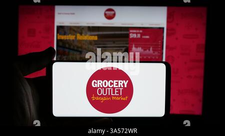 Stuttgart, Allemagne - 11-14-2024 : personne tenant un téléphone portable avec le logo de la société de vente au détail américaine Grocery Outlet Holding Corp. sur l'écran Banque D'Images