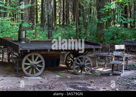 Vieux chariot avec un samovar moderne et tasse en acier se dresse au milieu des bois et des vieilles chaises. Banque D'Images