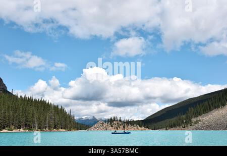 Les gens en canoë sur le lac bleu turquoise entouré de montagnes et ciel bleu avec des nuages Banque D'Images