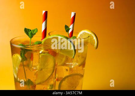 Deux verres d'un thé glacé avec des tranches de citron vert et de citron. La boisson est servie dans un verre avec des feuilles de menthe sur le dessus et des pailles blanches et rouges. Banque D'Images