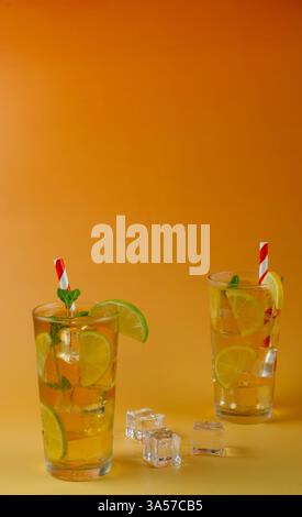 Deux verres d'un thé glacé avec des tranches de citron vert et de citron. La boisson est servie dans un verre avec des feuilles de menthe sur le dessus et des pailles blanches et rouges. Banque D'Images